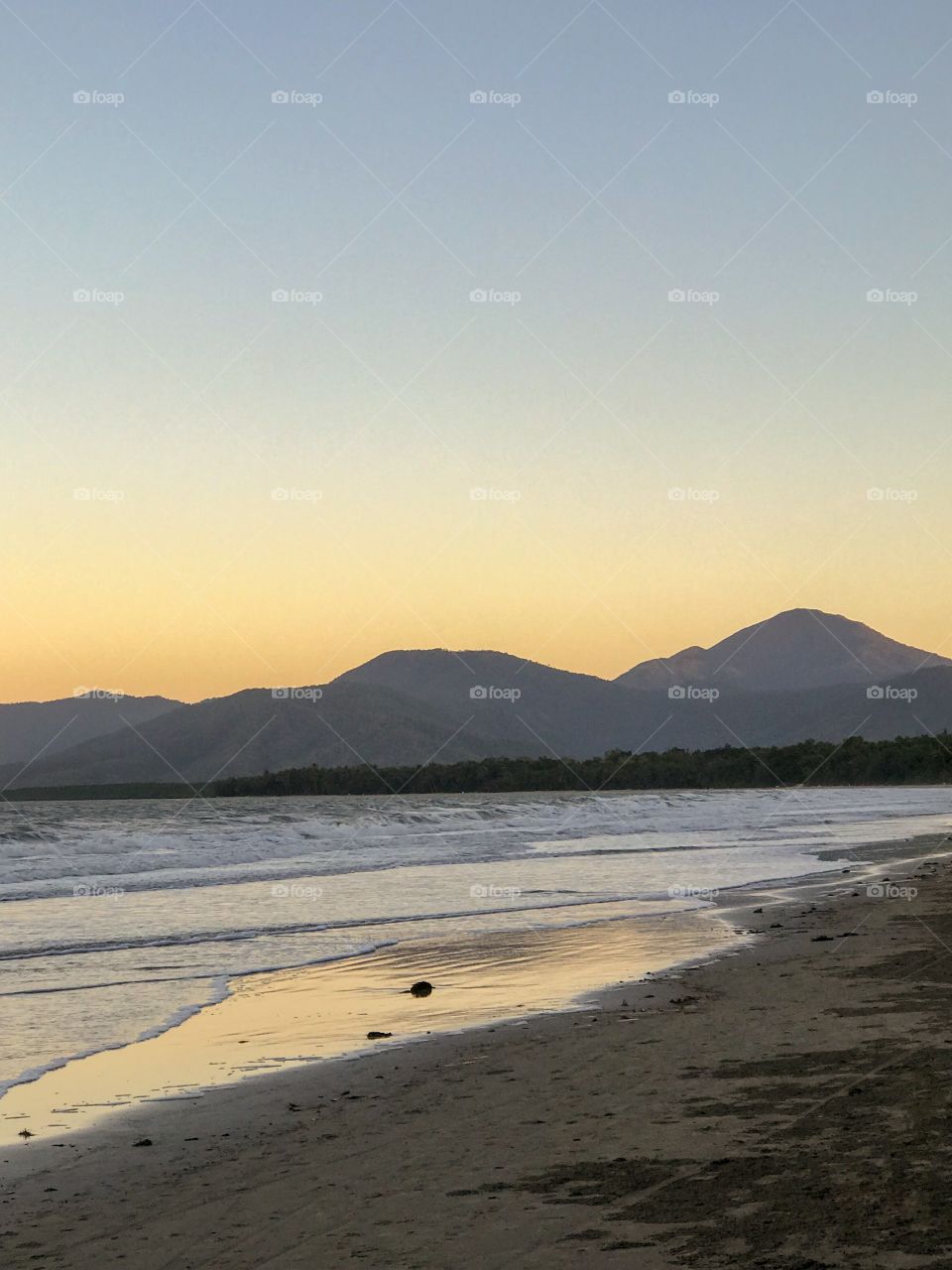 Sunset & reflections over calm & tranquil beach 