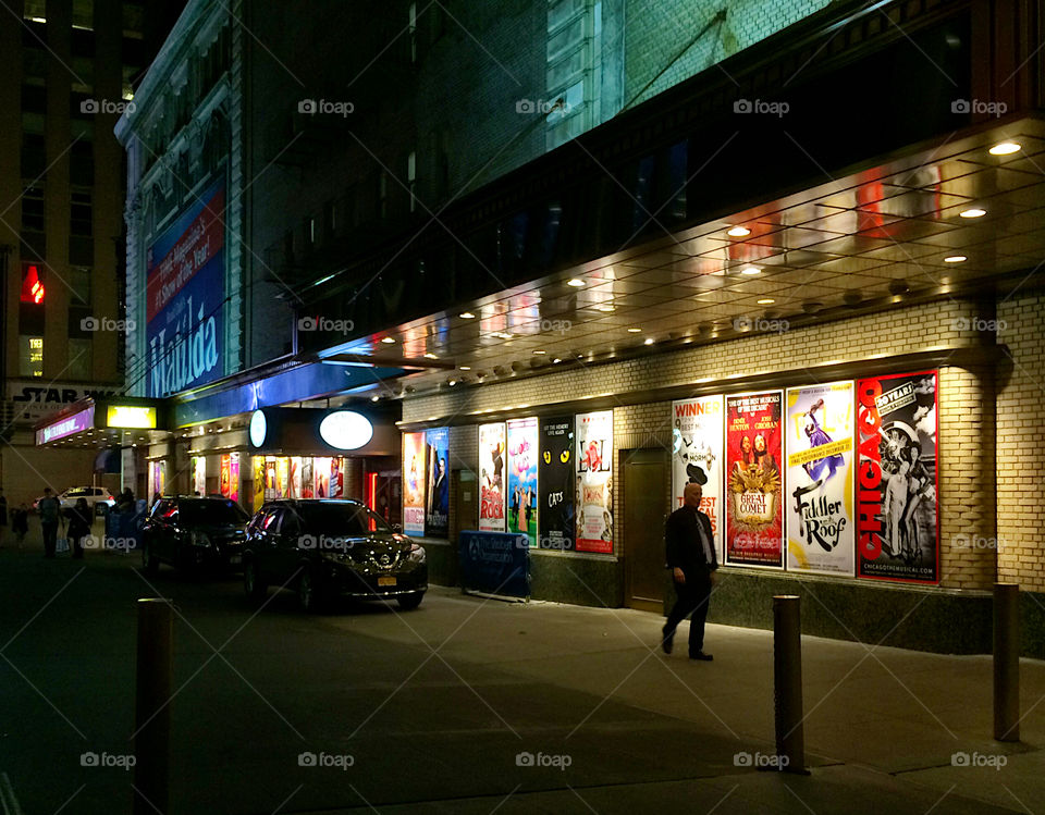 Lights are on in an alley next to a theatre. 