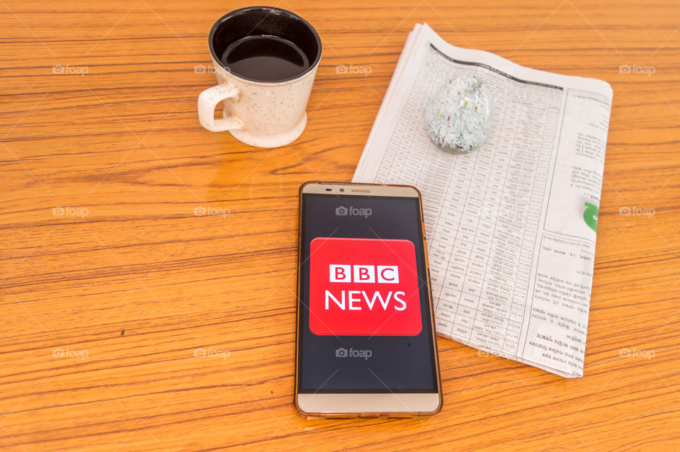 Kolkata, India, February 3, 2019: BBC news app (application) visible on mobile phone screen beautifully placed over a wooden table with a newspaper and a cup of coffee. A Technology Product Shoot.