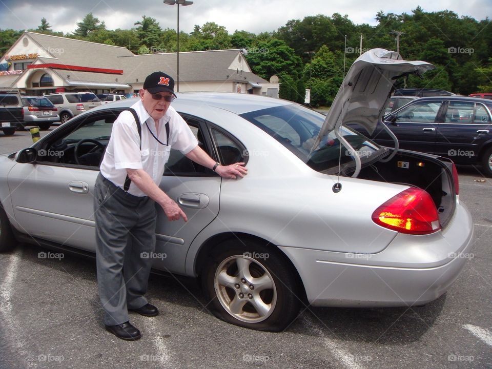 Senior man with flat tire in parking lot, waiting for help!