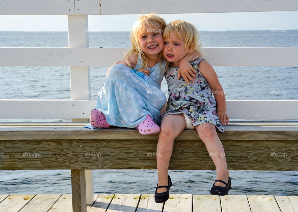 Two sister sitting on bench near sea
