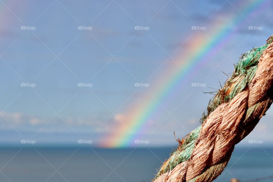 Nautical rope (closeup) arching foreground, bright rainbow arching over ocean background 