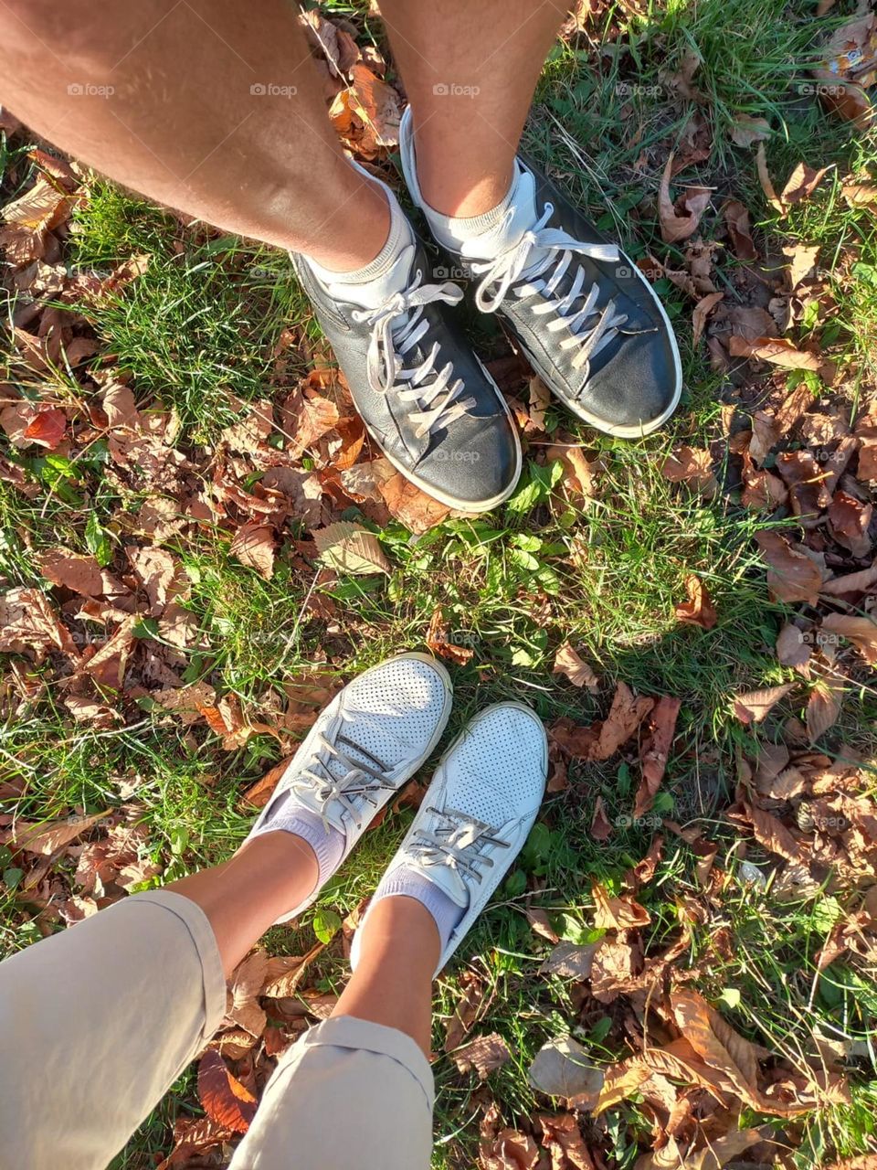 legs of a guy and a girl next to fallen leaves in the park