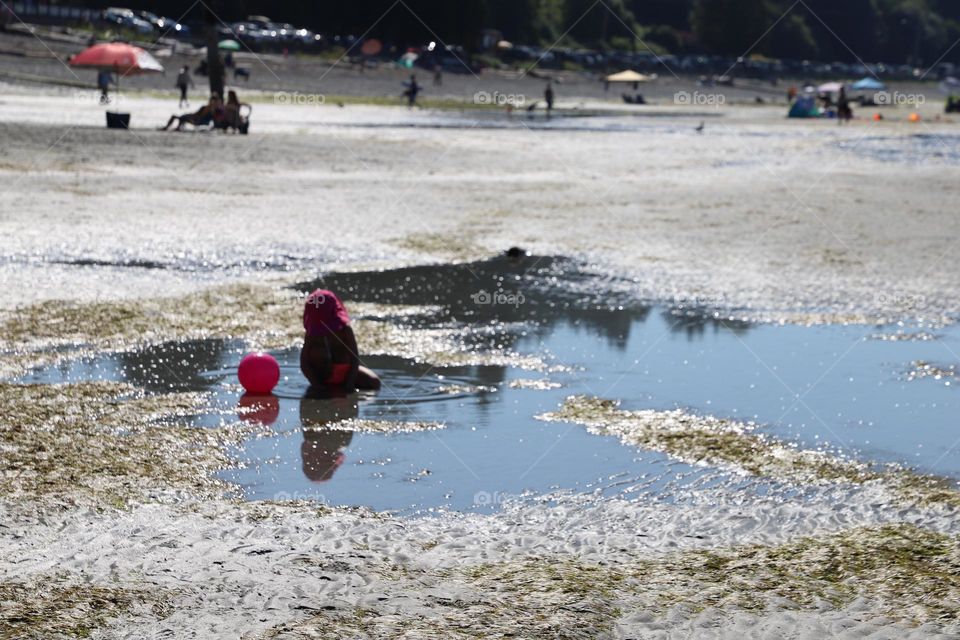 The girl with pink hat and pink ball playing in the puddle 