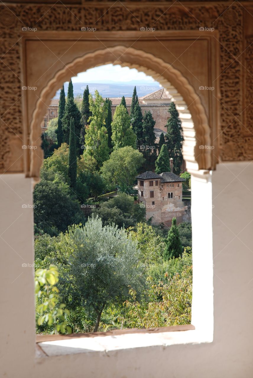 The gardens of the Alhambra through a small arch window in moorish style architecture