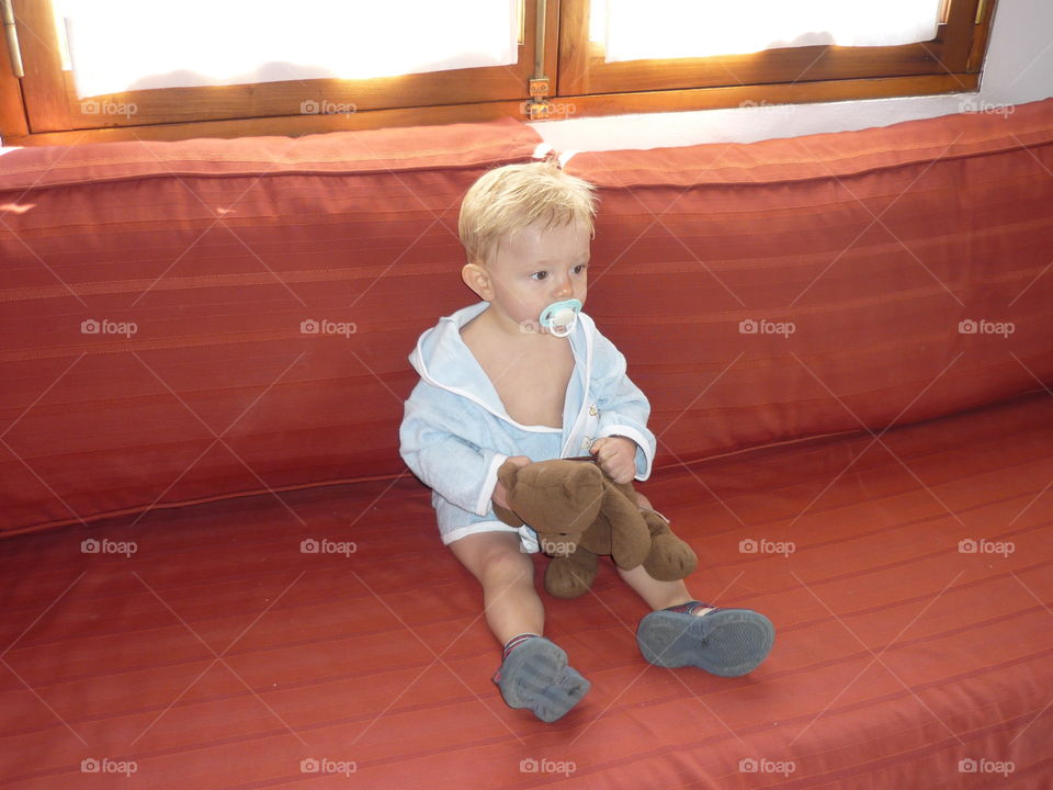 Baby with pacifier and teddy bear sitting on a couch