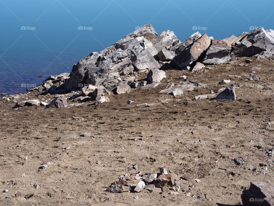 Jagged rocks and boulders along the shoreline of Ochoco Lake in Central Oregon on a sunny spring day.