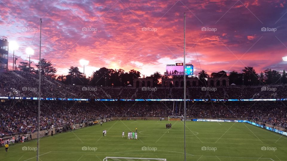 Beautiful scenic pink and purple sunset over a soccer field and crowded stadium in the evening