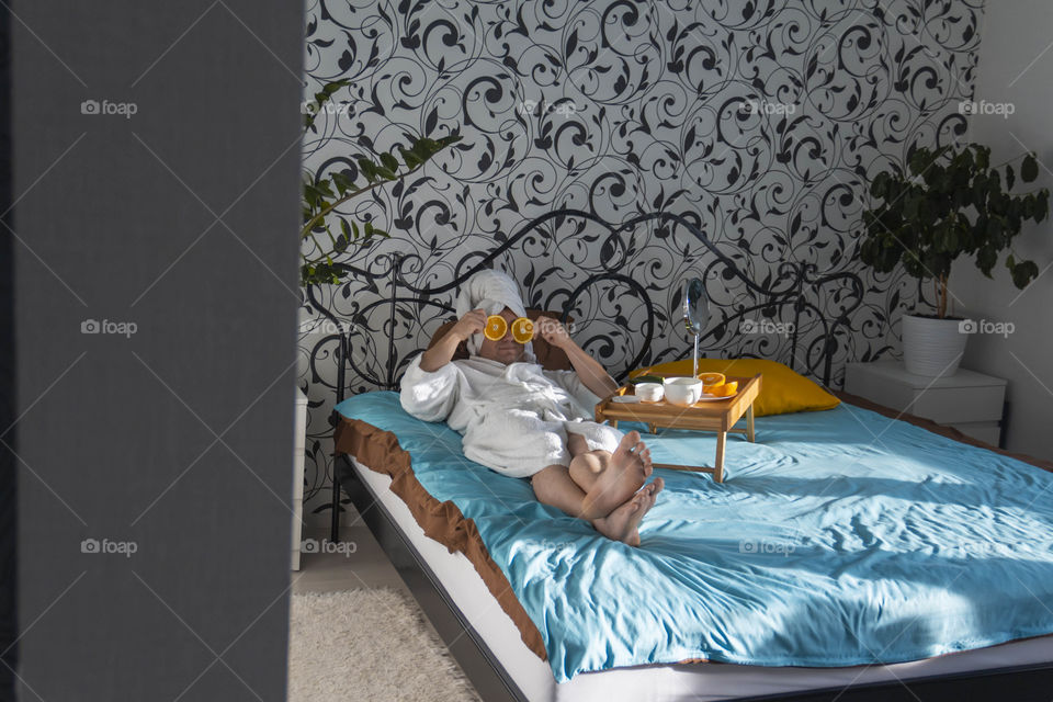 A man and home spa care at home takes care of himself and smears his face with cream, does a manicure at home on a blue background and with oranges and rests.