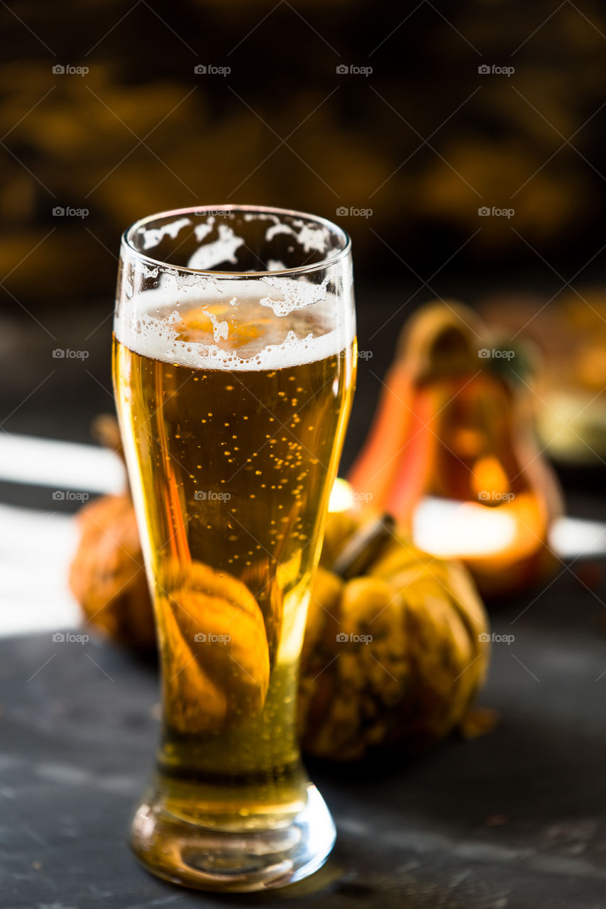 golden beer in a glass on rustic, black table next to autumn decorations