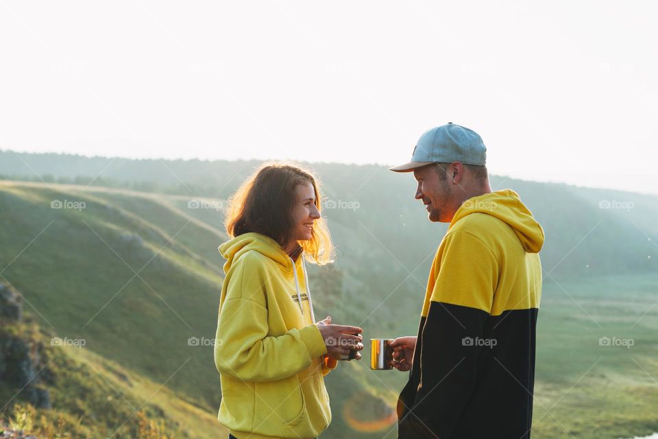 Young happy family couple travelers in casual outfits with tea in morning on beautiful view background. Local tourism, weekend trip