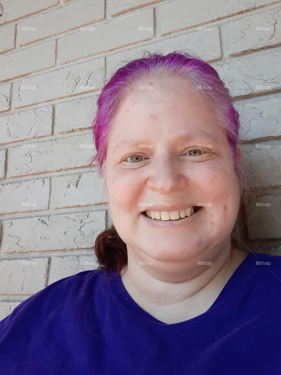 I took this selfie while getting some fresh air outside. I have purple hair and a smile on my face.