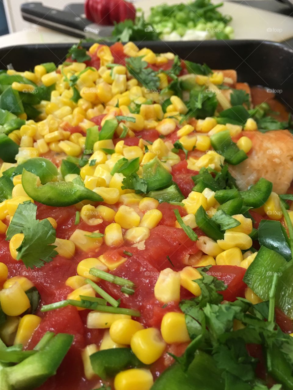 Minced beef enchiladas in baking pan, topped with corn, cilantro, tomatoes, enchilada sauce and cheese healthy and colourful Mexican food!