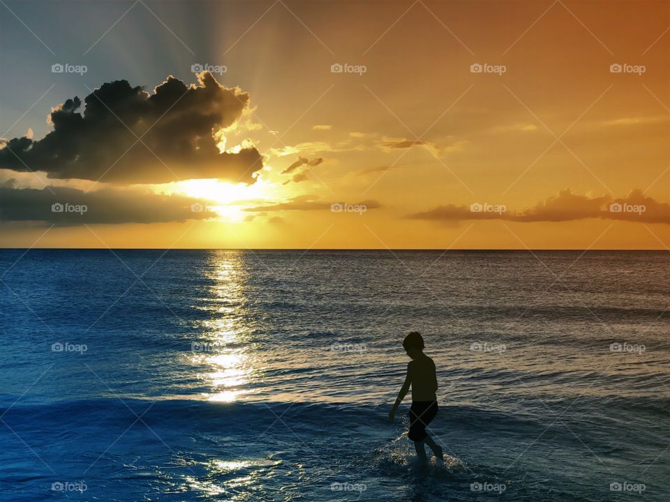 A radiant golden sunset and a beautiful blue ocean harmonize with a small boy.