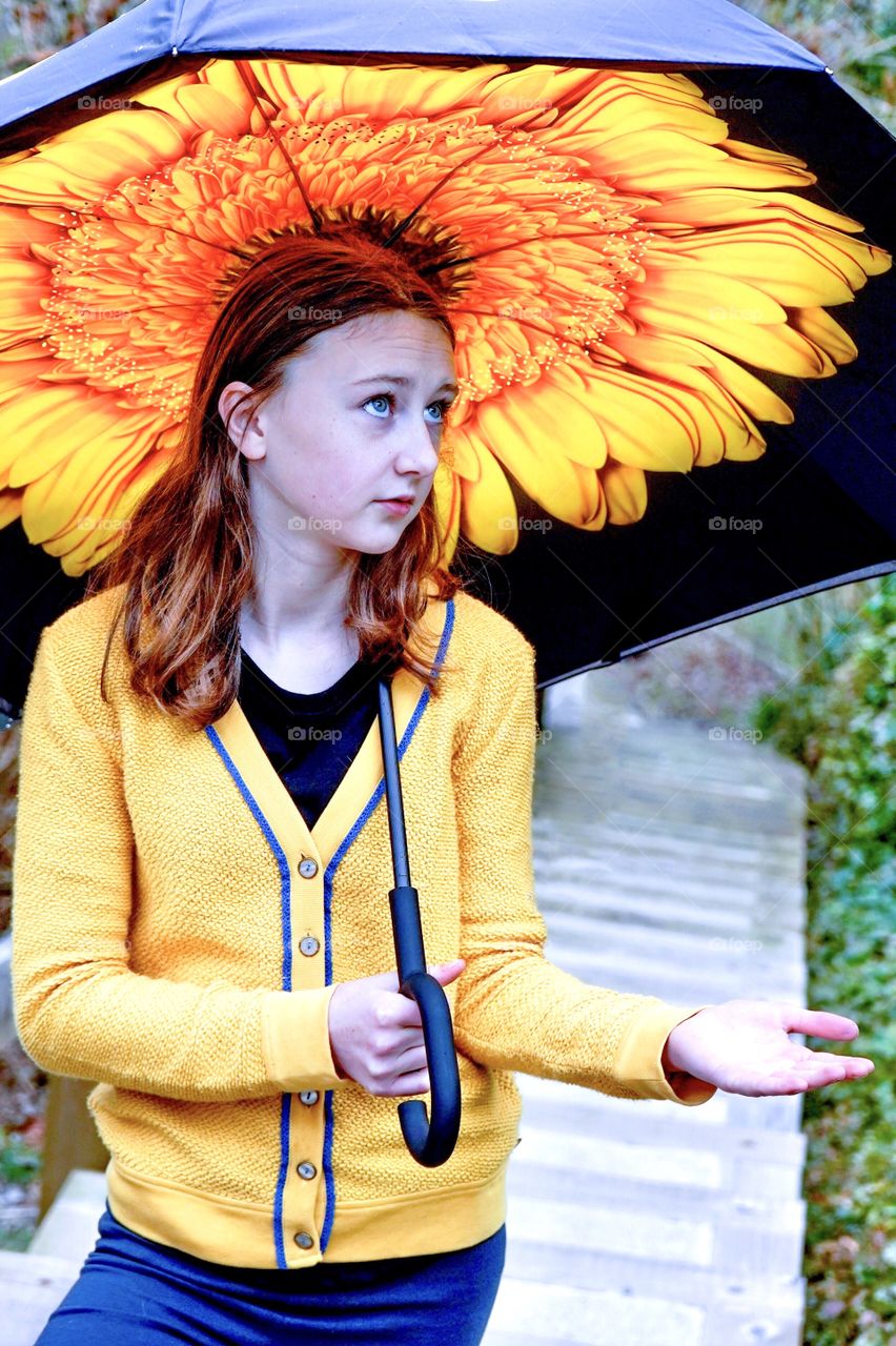 Girl checks for raindrops from under her big yellow umbrella 