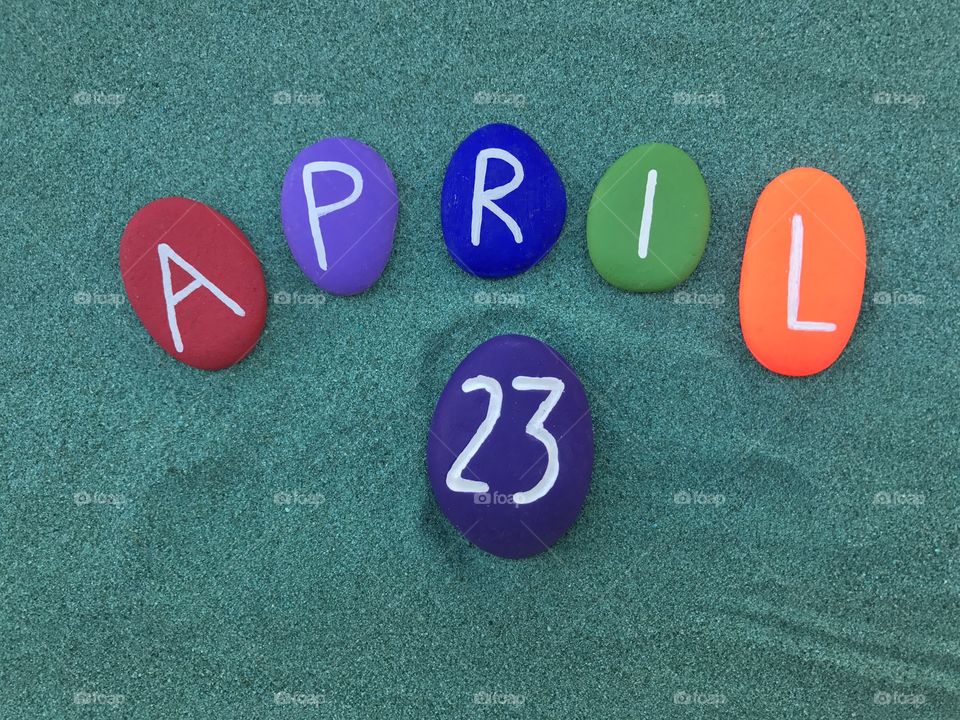 23 April, calendar date with colored stones over green sand 