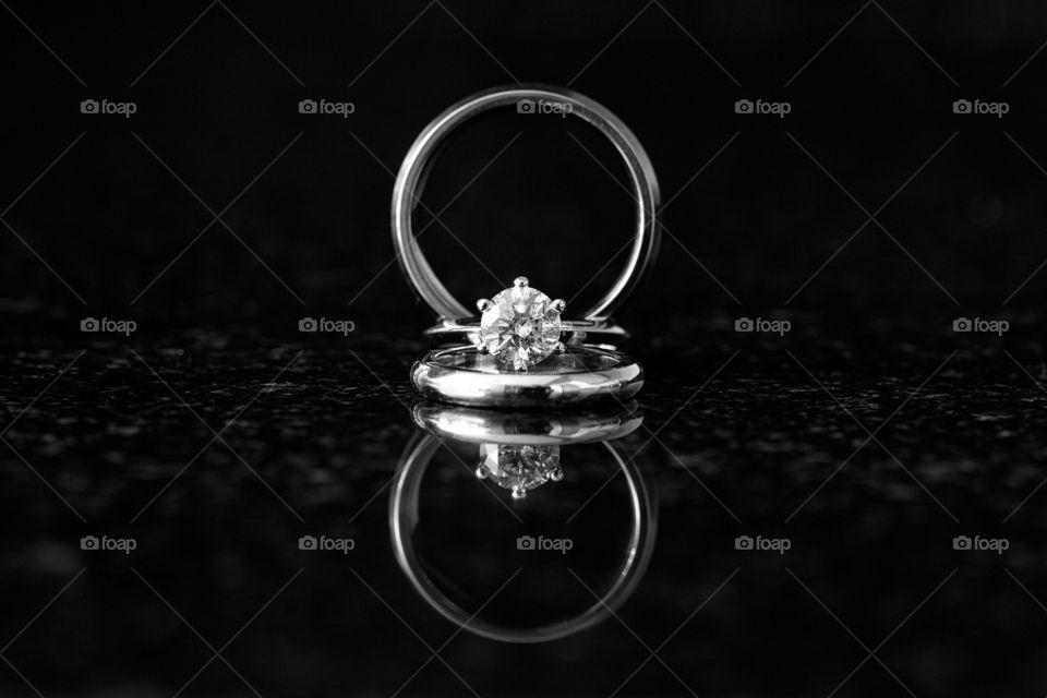 Wedding bands and close up of diamond rings on black reflective surface. Black and white macro image