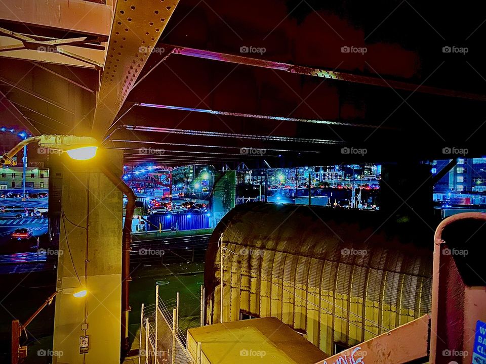 From a lower level of the staircase descending to the parking lot beneath the “Pulaski Bridge” in LIC, Queens at “Newtown Creek”. The red metal roof seen from beneath is the structure that supports the bridge. 2023. Hypnotic Productions