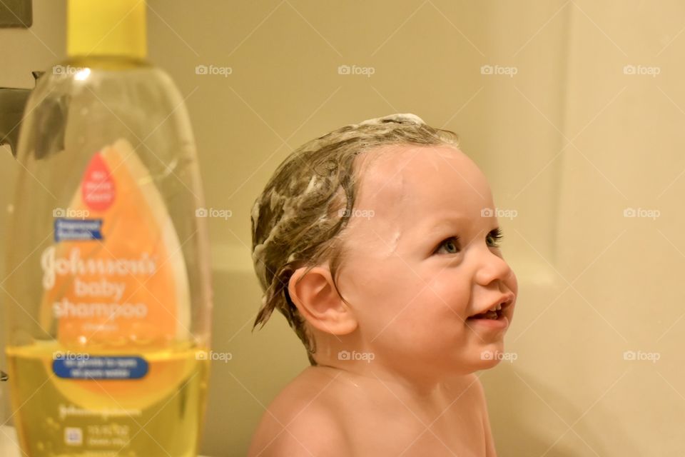 Cute toddler boy having fun in bath and washing his hair with Johnson’s baby shampoo 