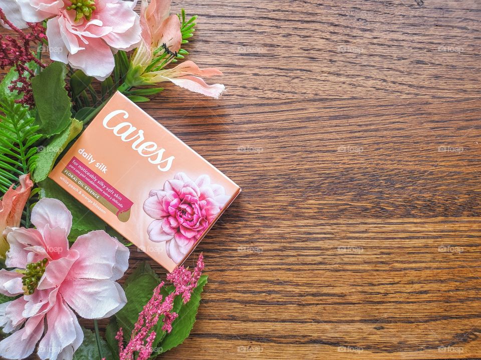 Right side oriented:  The new look Caress bar single pack of daily silk on a wood surface accented with complementary florals.
