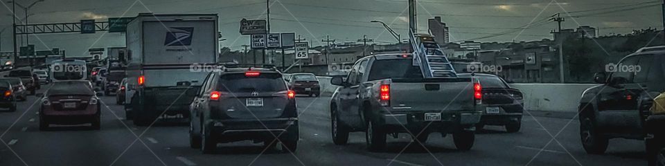 Commuting in traffic at sunset as storms set in with glimpse of sunlight peering through the clouds.