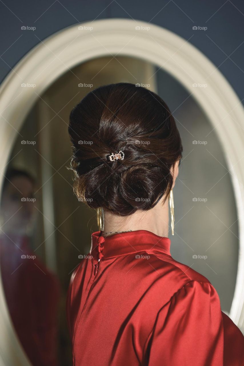 A beautiful girl in jewelry and a red dress looks in the mirror