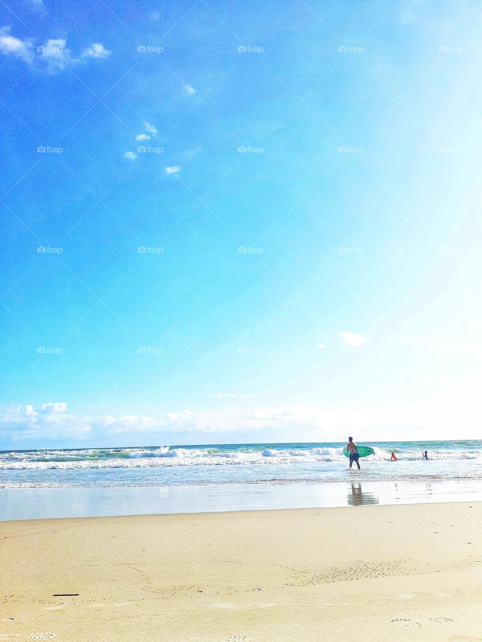 A surfer carries a surfboard into the ocean for a day of surfing at Ponce Inlet Beach in Ponce Inlet, Florida.