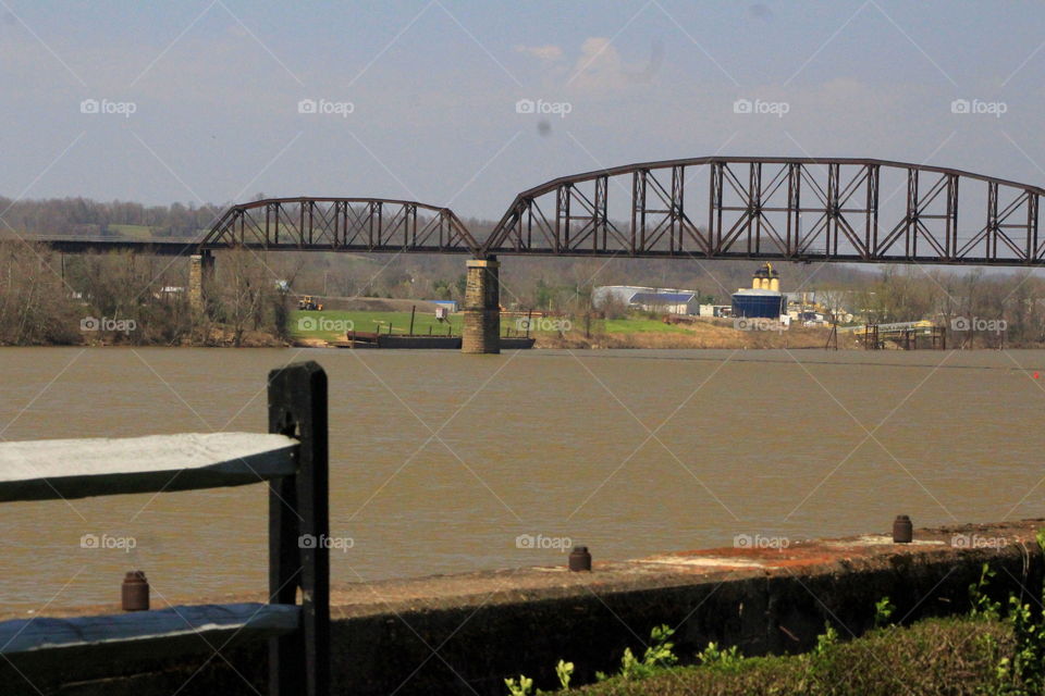 This is a picture of a train track bridge going over the Ohio River on a cool spring sunny day.