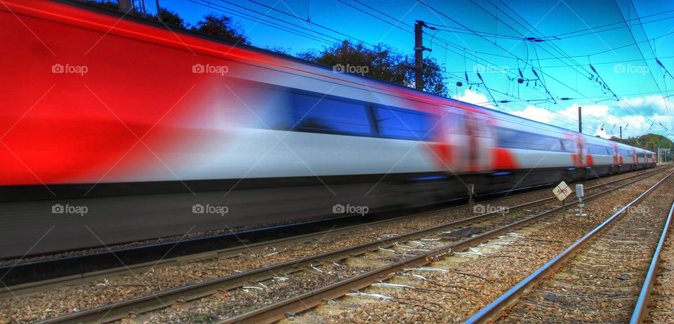 A passenger express train speeds past underneath electric wires and is blurred by motion blur.