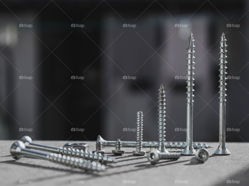 Screws and bolts of various sizes lie geometrically on a stone step on a sunny day in a blurred backyard, close-up side view. The concept of tools,metal, construction, repair.