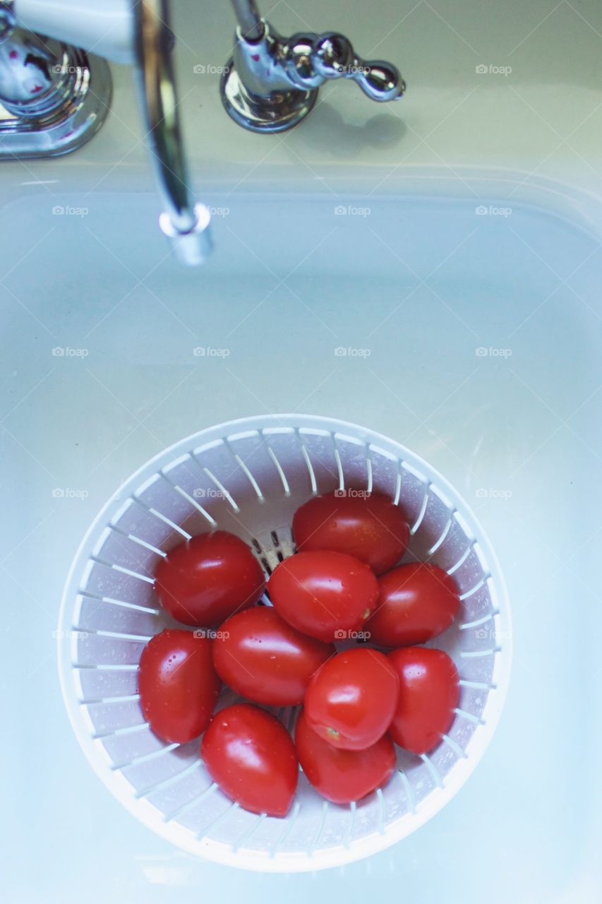 Roma tomatoes in a white colander in a white sink, white vintage-style faucet handle and  chrome filtered water spigot 