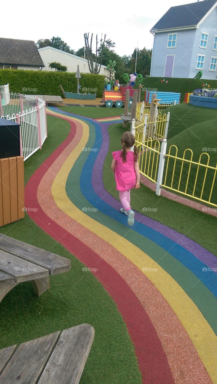 girl running down rainbow road in play park