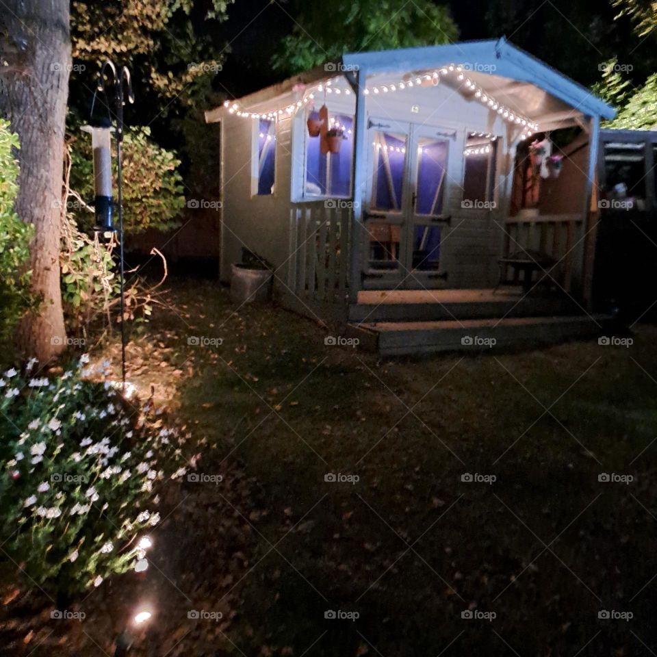 nightime garden with summerhouse and foliage lit up with fairylights. dark.