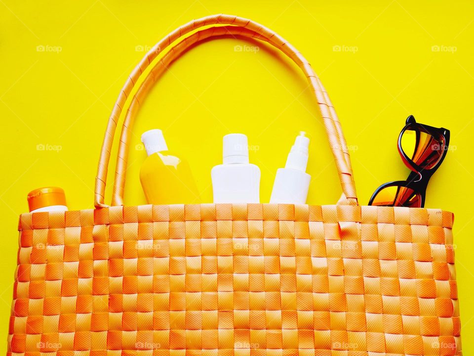 flat lay with orange beach bag and sunscreen on yellow background