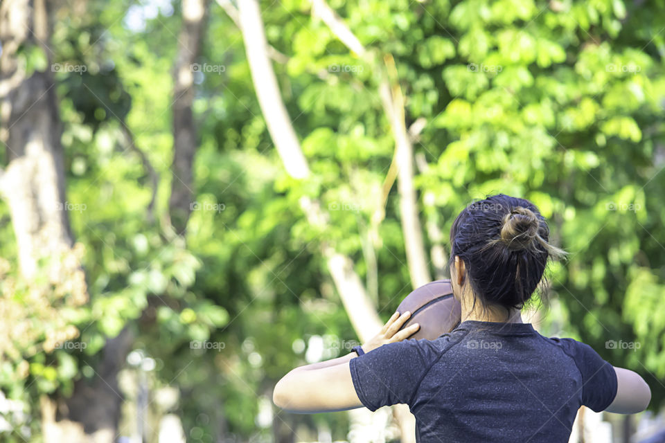 Asian Woman holding basketball Background blur tree in park.