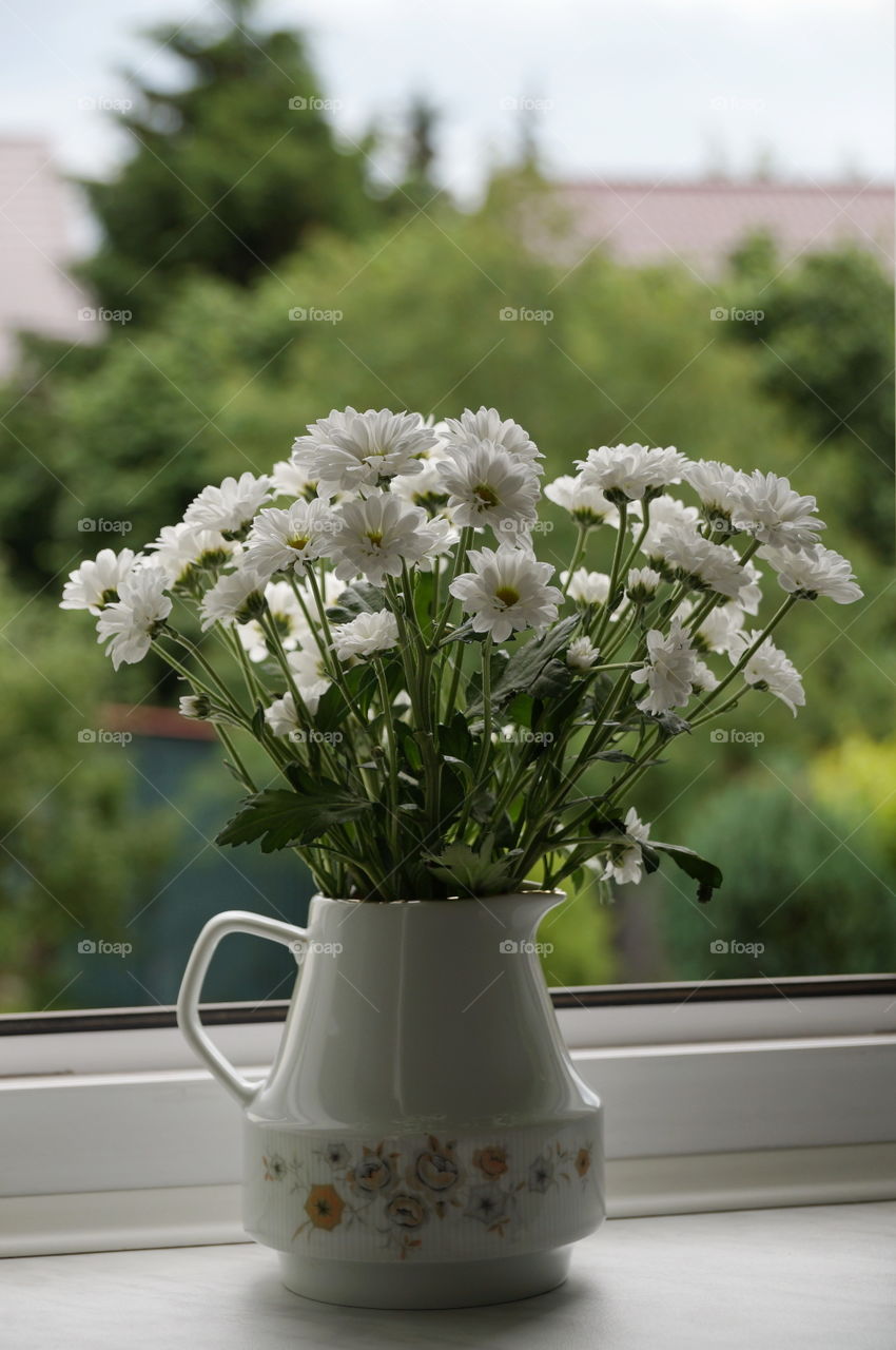 Bouquet of white chrysanthemum flowers in a vase on the windowsill