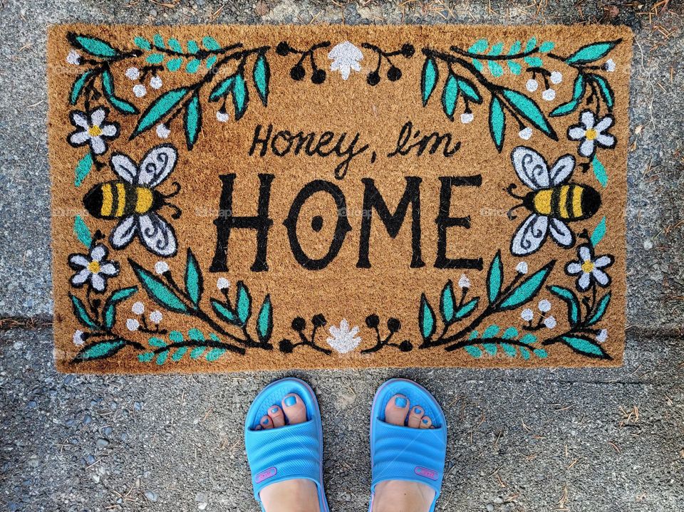 Feet in blue sandals waiting to step on the honey I'm home welcome mat.