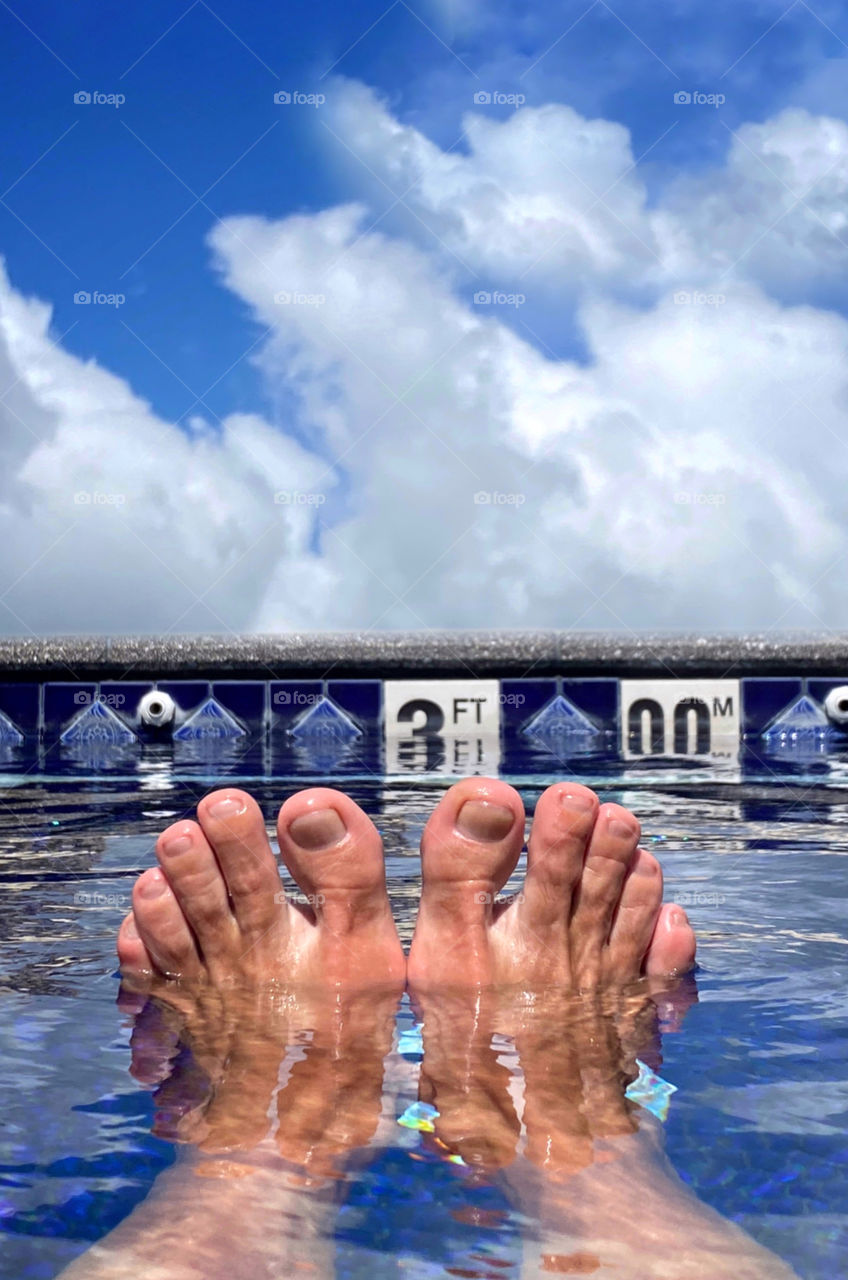 Two feet sticking out of the water at the shallow 3-foot end of an outdoor swimming pool 