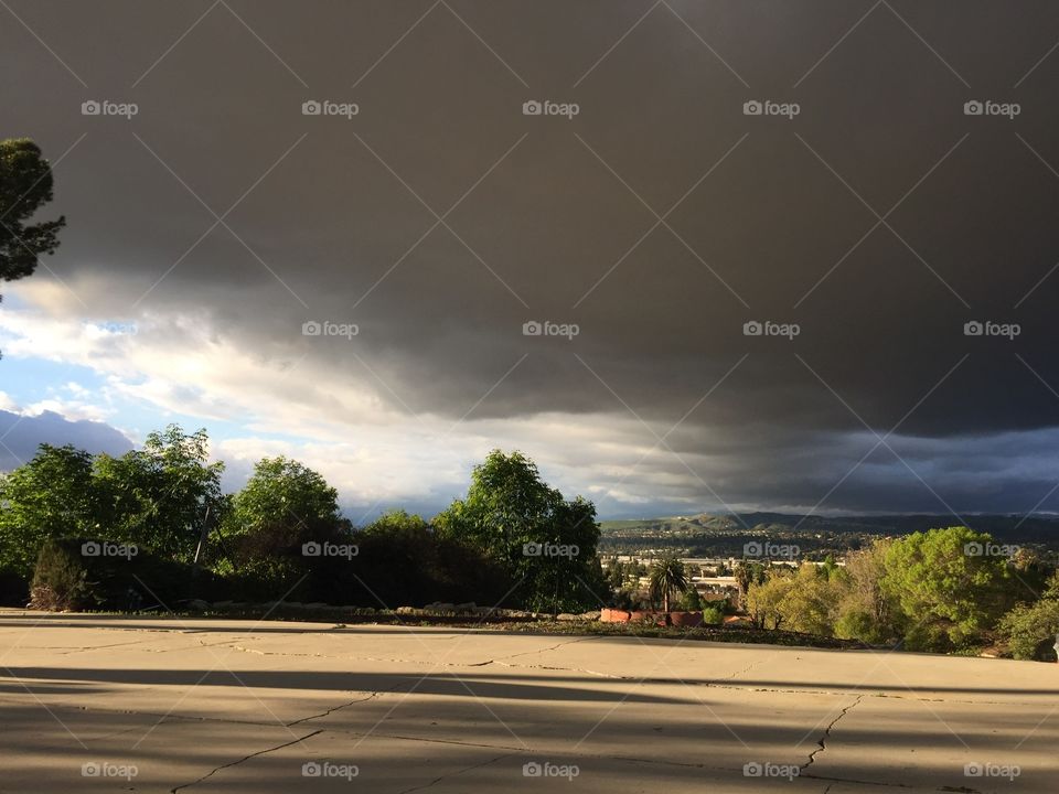 Dark sky with clouds about to rain. Sunlight coming from left side. Trees and concrete in landscape. 