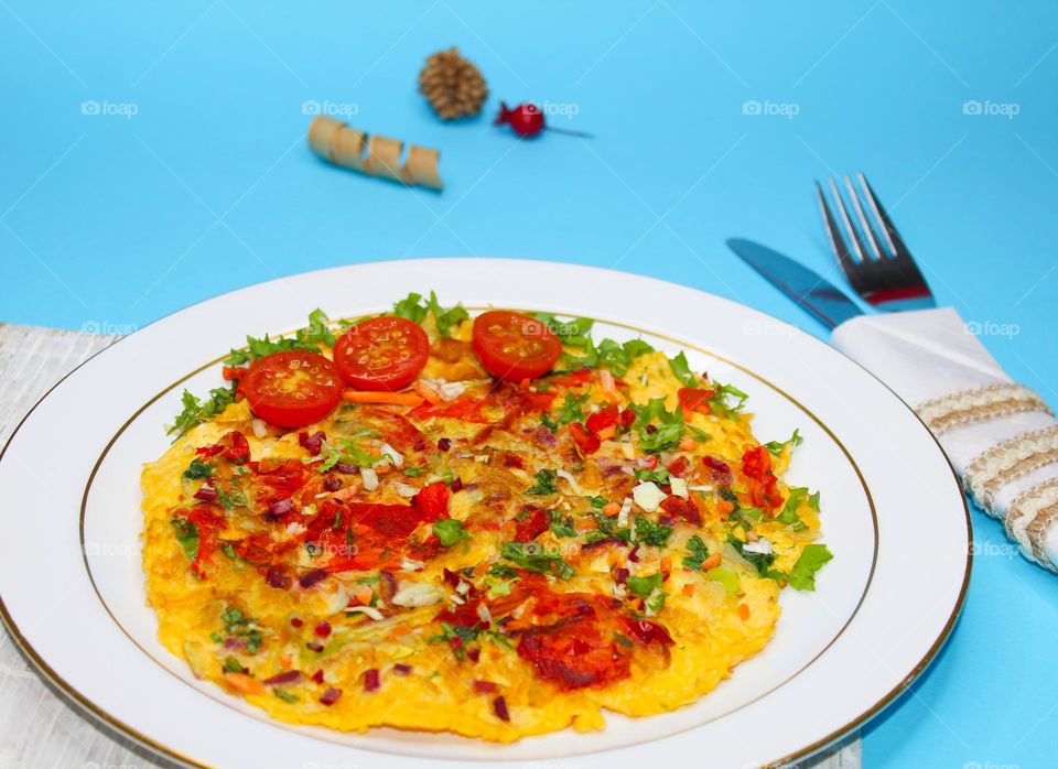 Omelet with vegetables on a white plate.  Blue background with napkin,  knife and fork