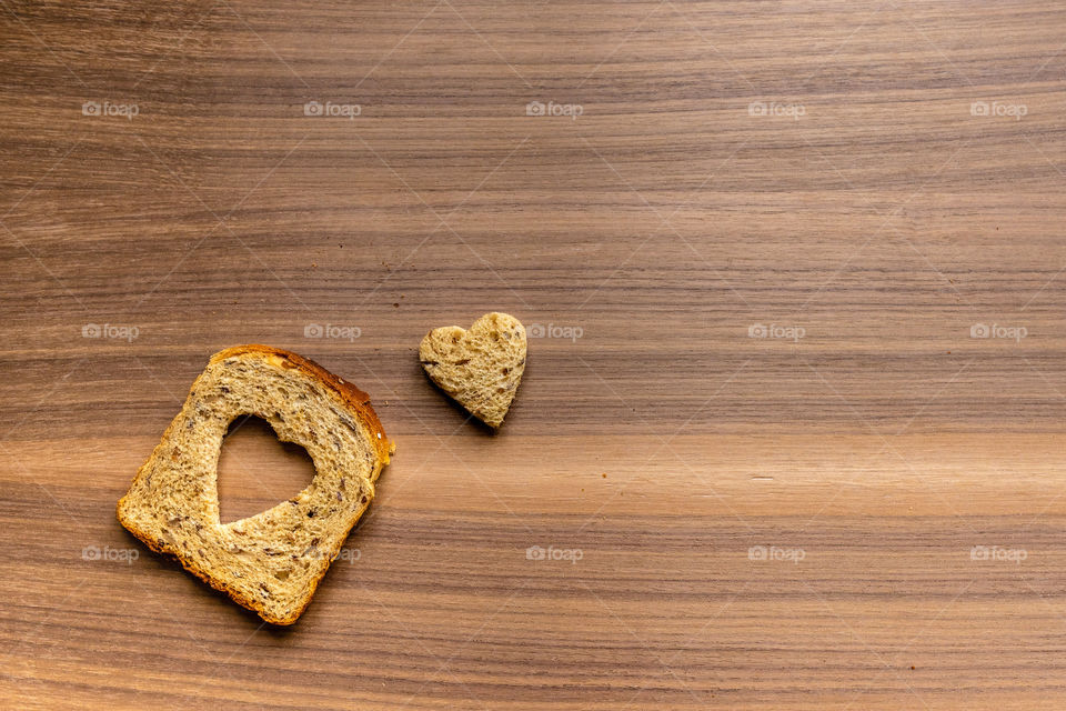 Bread with heart-shaped cut and heart from bred. Wooden texture background.