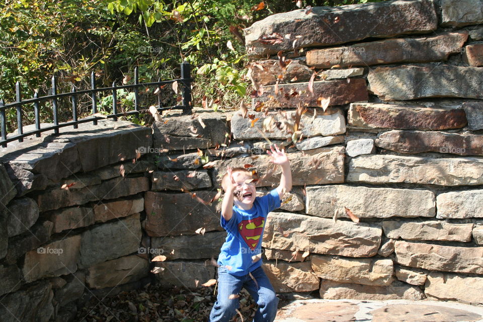 Happy boy playing with dry leaves in park