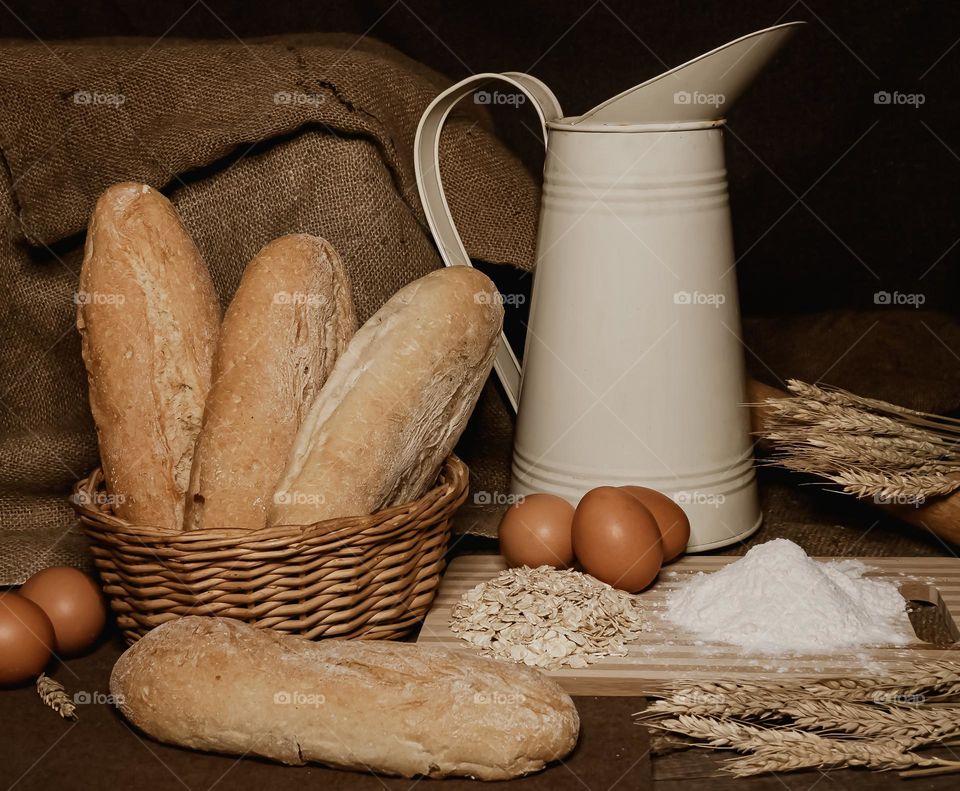 Still life of bread, eggs, flour, milk and oats against a sackcloth background 