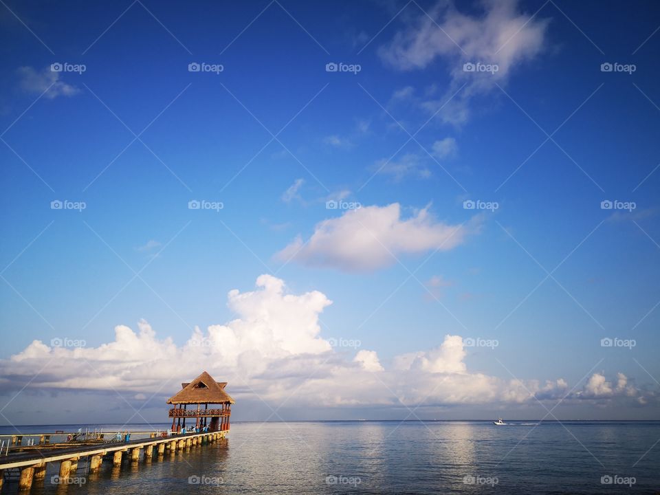 Muelle en Cozumel, aquí apreciamos la belleza de la naturaleza, océano tranquilo, cielo azul y esponjosas nubes que se reflejan en las calmadas aguas, tan relajante y hermosos, bello cuadro que encontramos en Cozumel Quintana roo