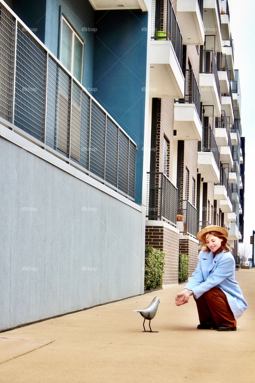 A young woman offering food to a bird in an urban setting on a bright sunny day!