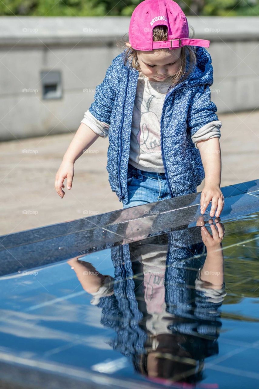 Cute girl looking at her reflection in water