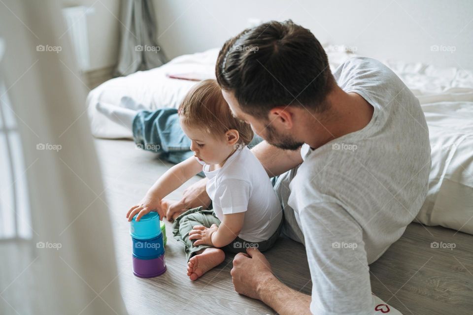 Happy father young man and baby girl little daughter having fun playing with toy in children room at home