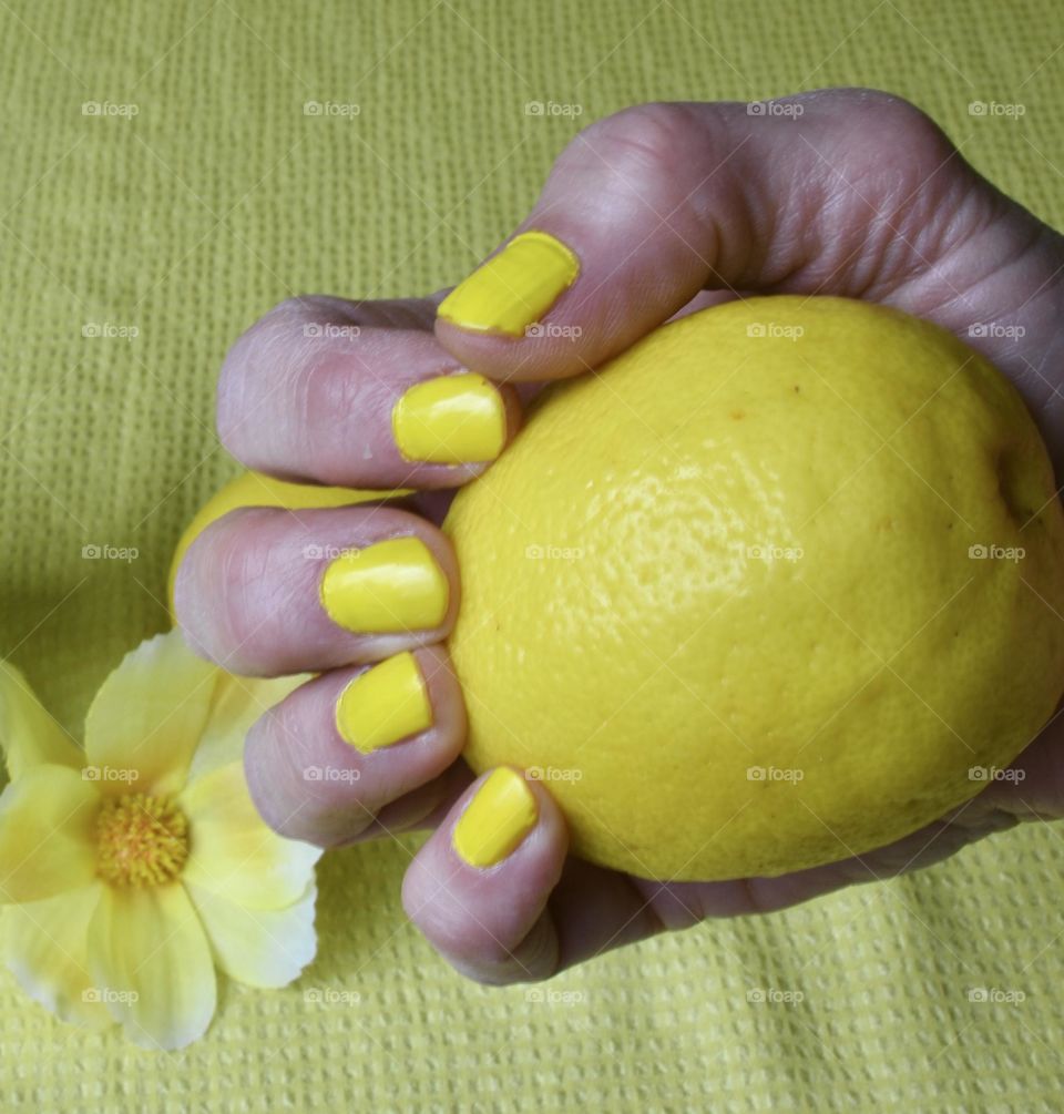 Woman with yellow nail polish holding a lemon