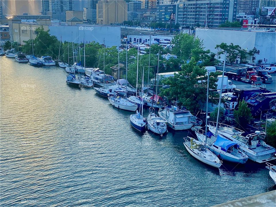 The setting evening sun is reflecting in the water of the “East River” at “Newtown Creek” underneath the “Pulaski Bridge” in LIC, Queens and a great variety of boats can be seen tied to the shore. 2023. Hypnotic Productions
