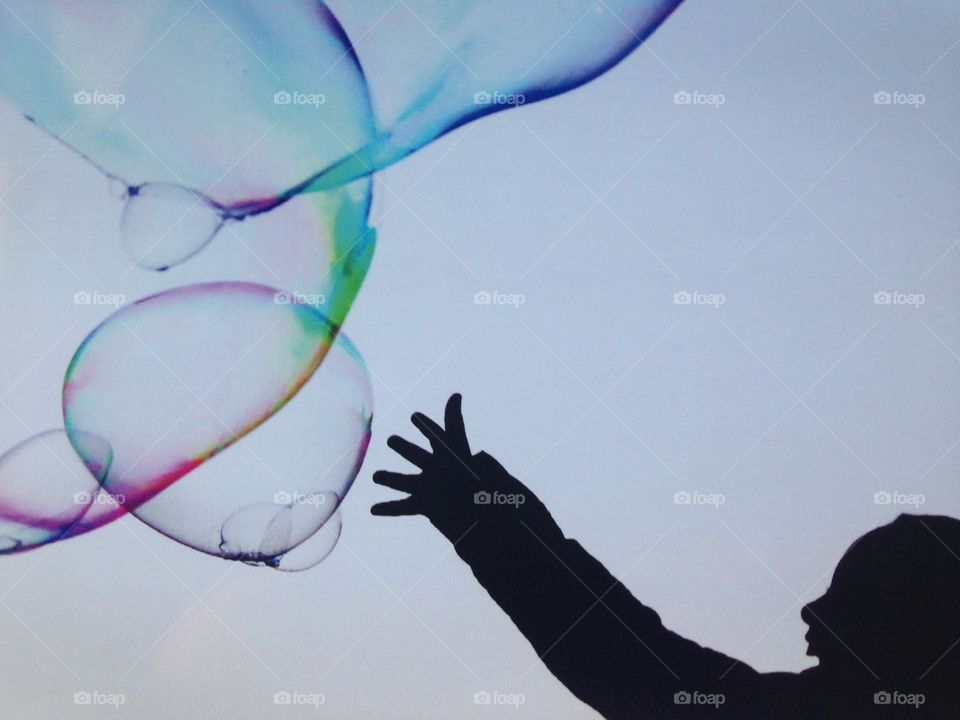 Silhouette of child reaching for soap bubbles 